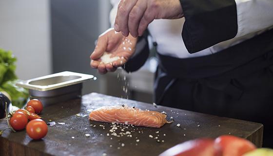a chef seasons a fresh salmon filet