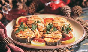 Grilled salmon steaks on a plate with lemon and tomato slices.